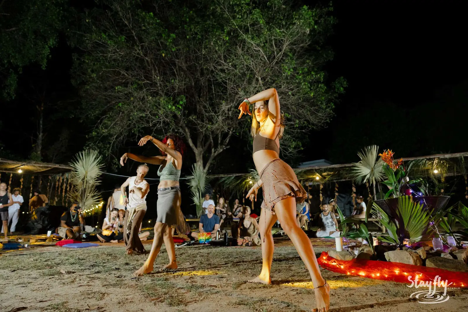 Dancers move freely near fire ring at dusk.