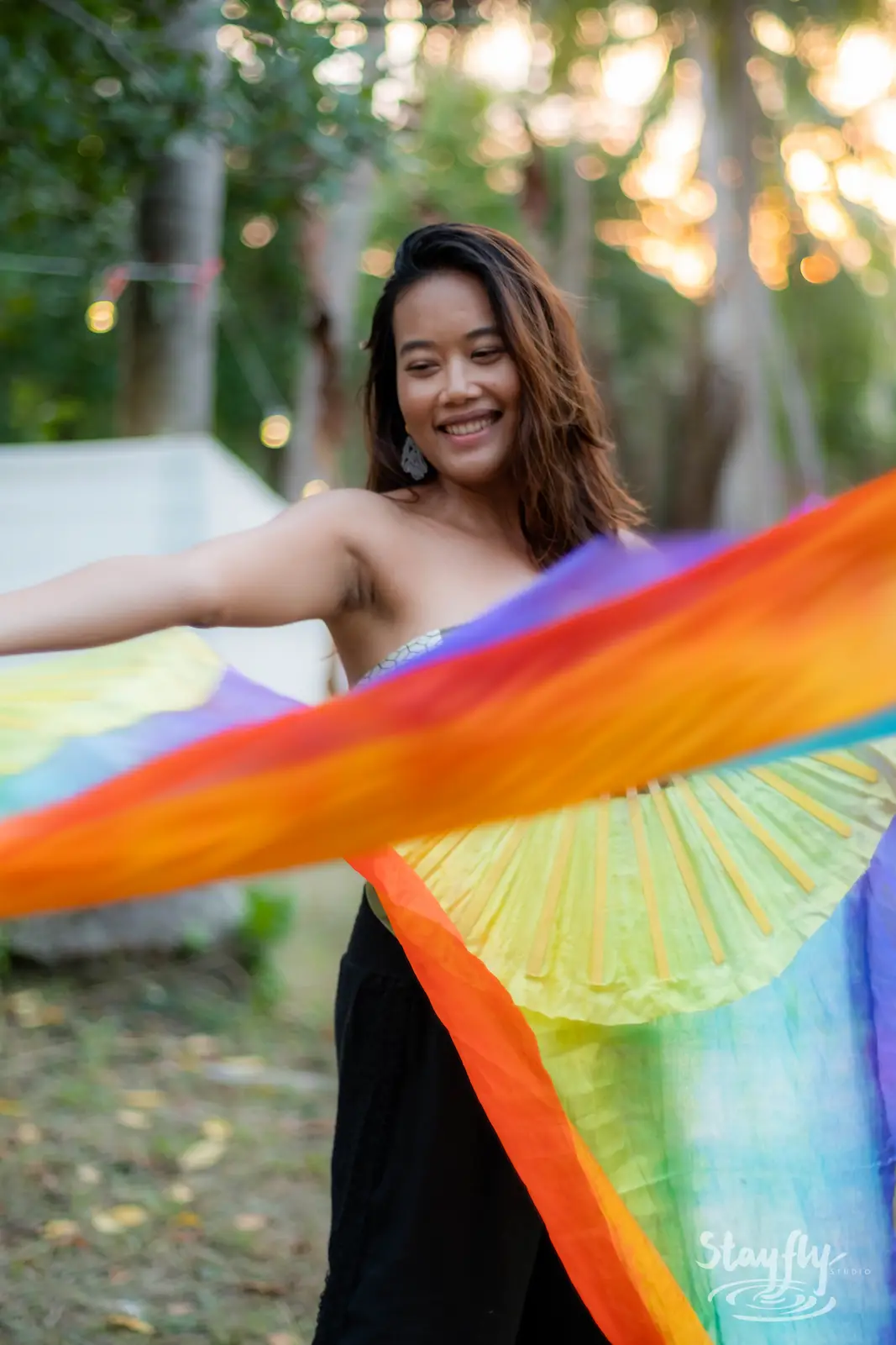 Woman twirling rainbow fabric outdoors at dusk.