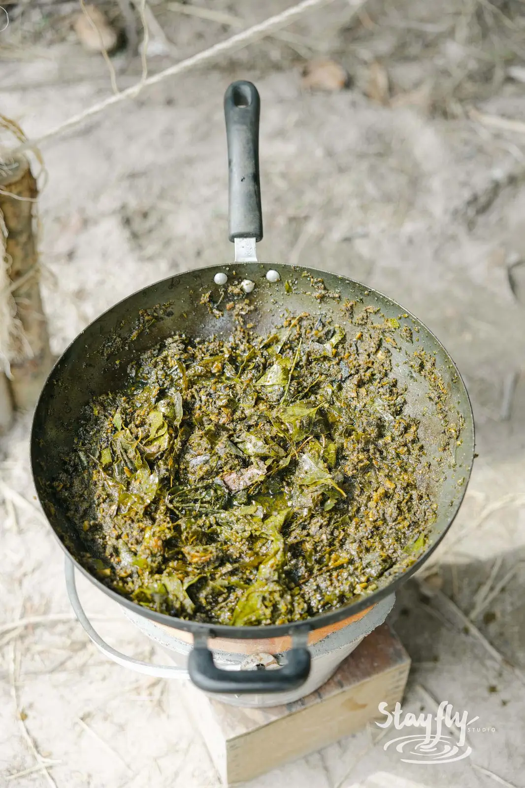 Wok of cooked leafy greens on outdoor stove.