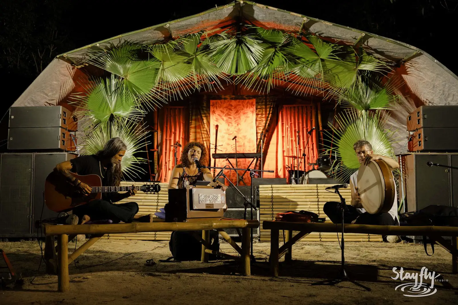 Trio performing under palm-thatched stage canopy.