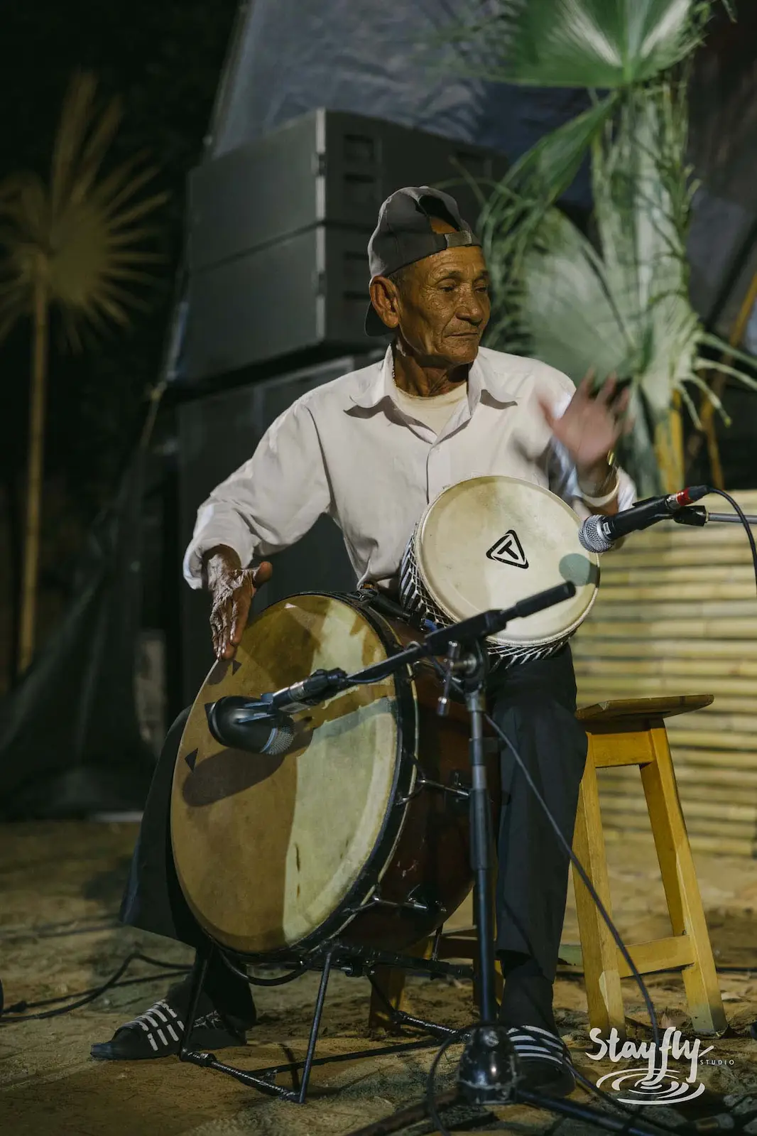 Elderly man playing hand drums on stage.