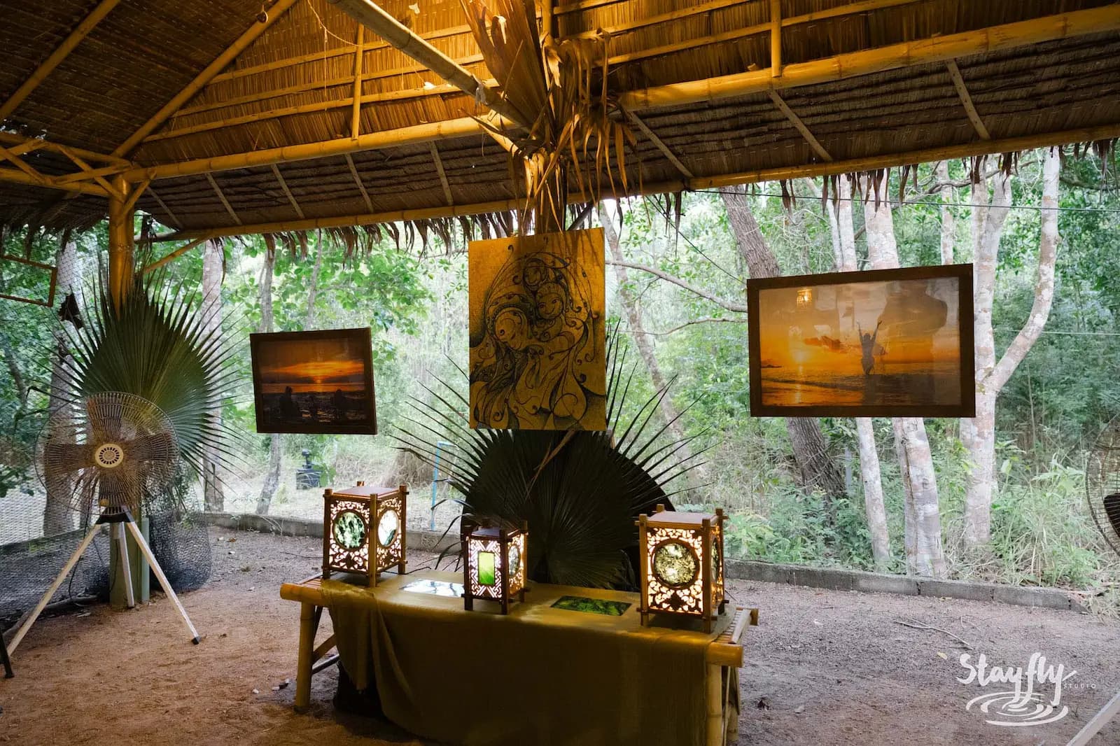 Photo prints and lanterns displayed under thatched roof.