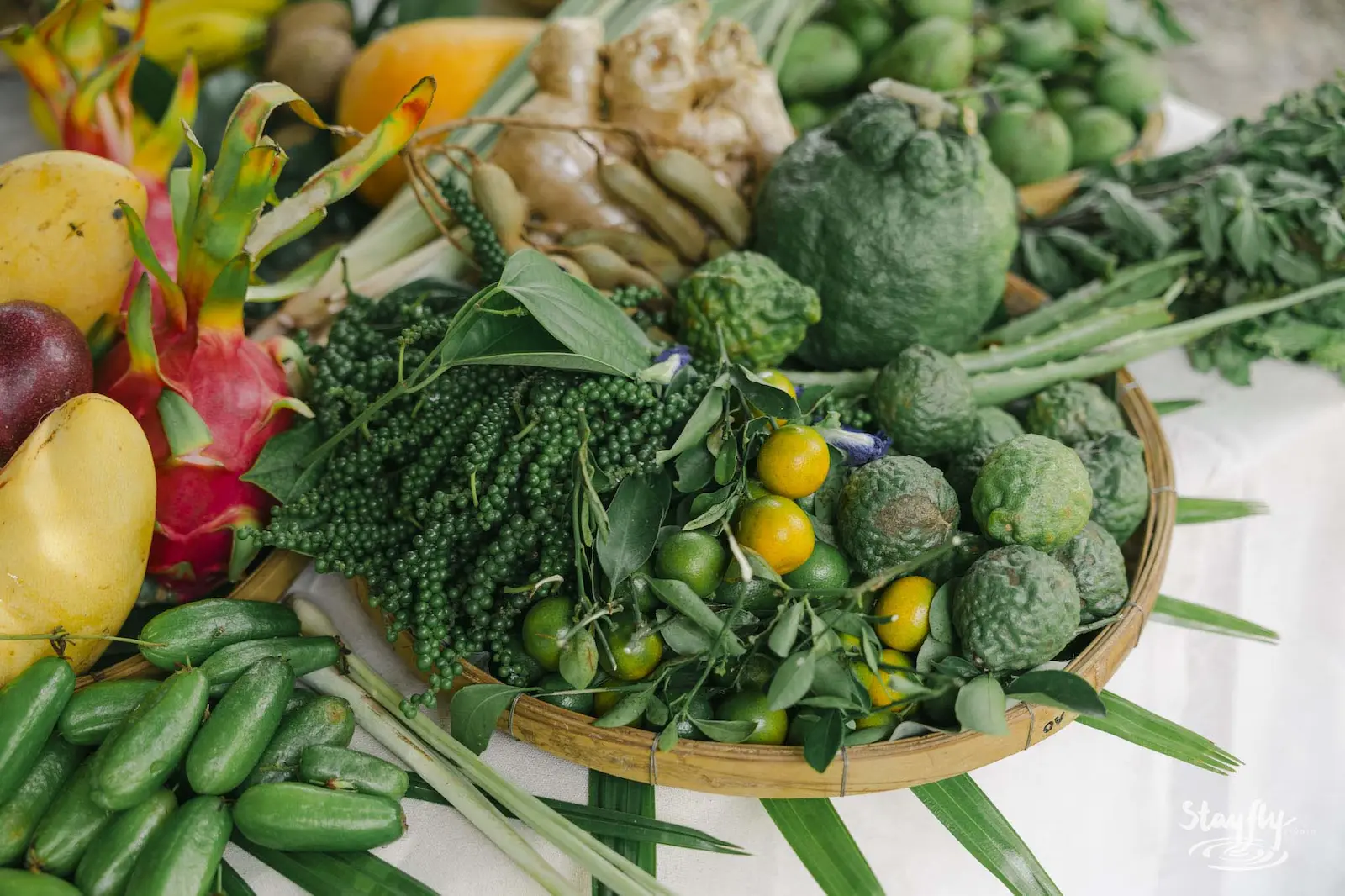 A woven tray filled with green vegetables beside a display of fruit.