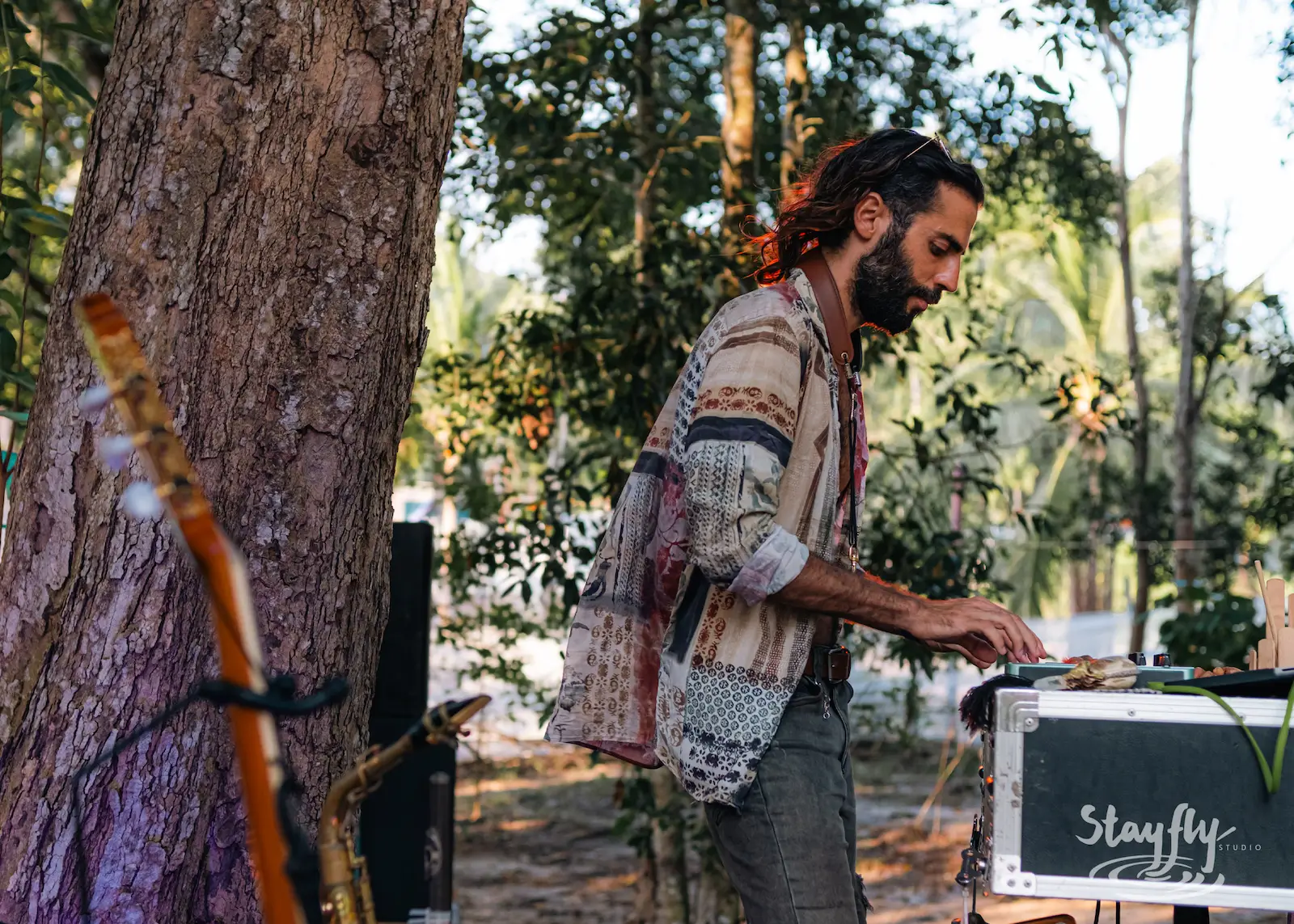 Man adjusts sound equipment near tree.