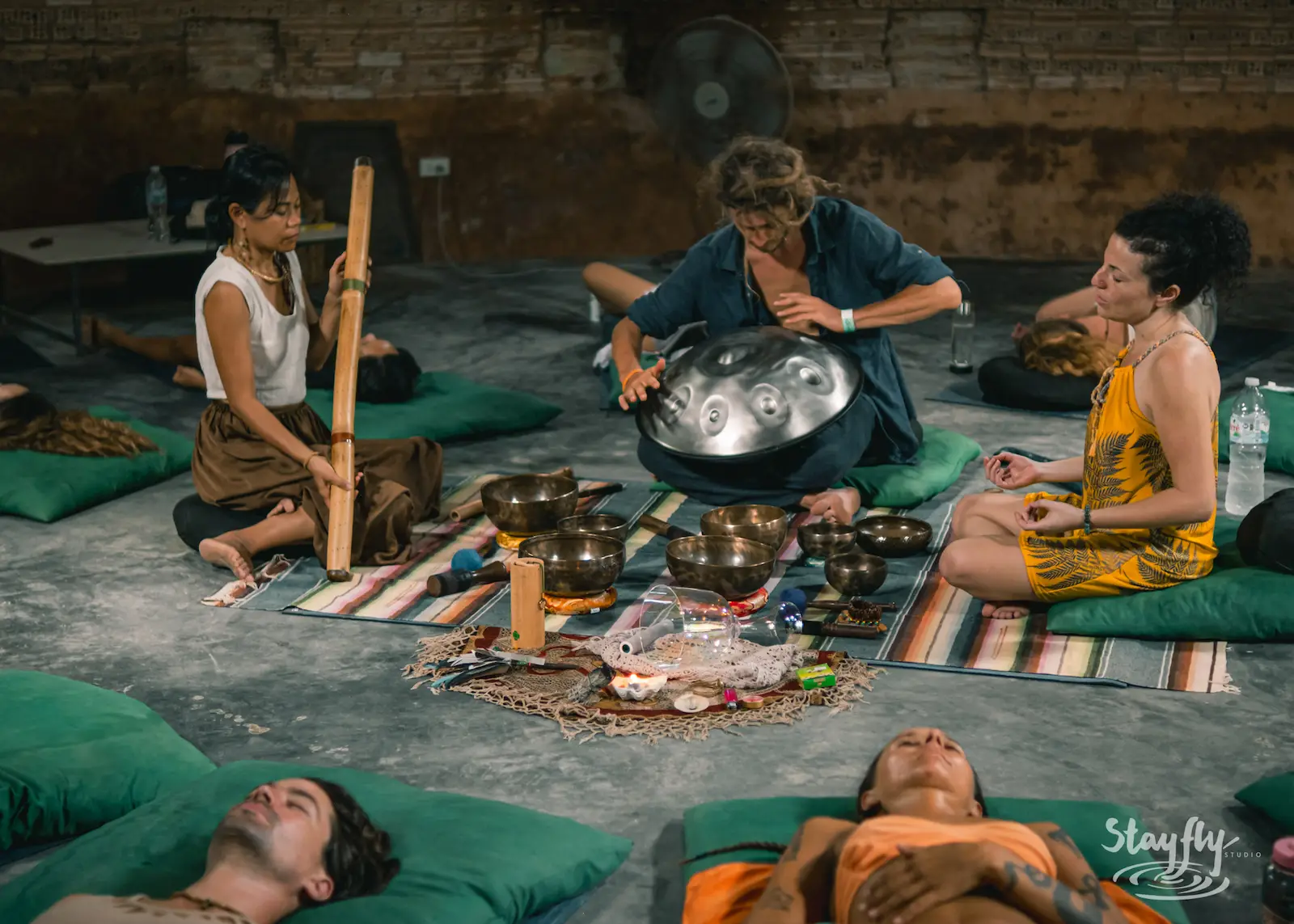 A bamboo flute and a handpan played side by side while people rest on mats around them.