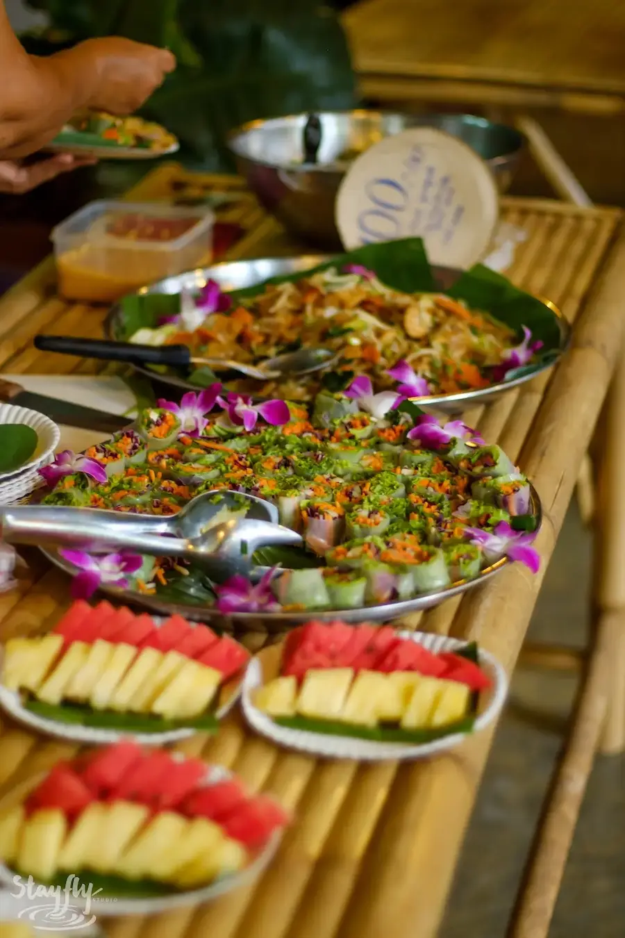 A platter of fruit and salad laid out on a banana leaf tray with flowers.