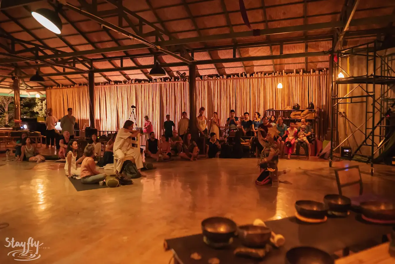 The pavilion at evening, warm light on participants seated around a practitioner and a gong.
