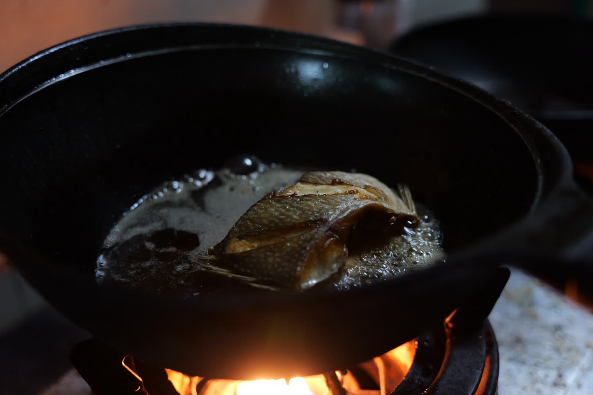 A whole fish frying in a wok over a flame.