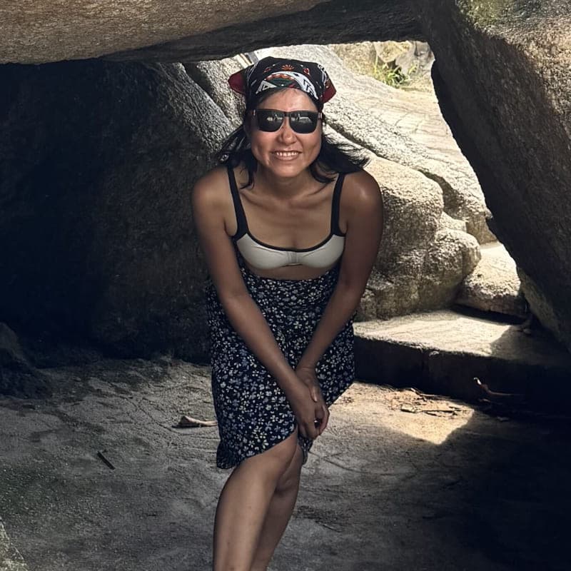 Panyasiri Kiatmahakun smiling beneath a boulder arch, in a headscarf and sunglasses.